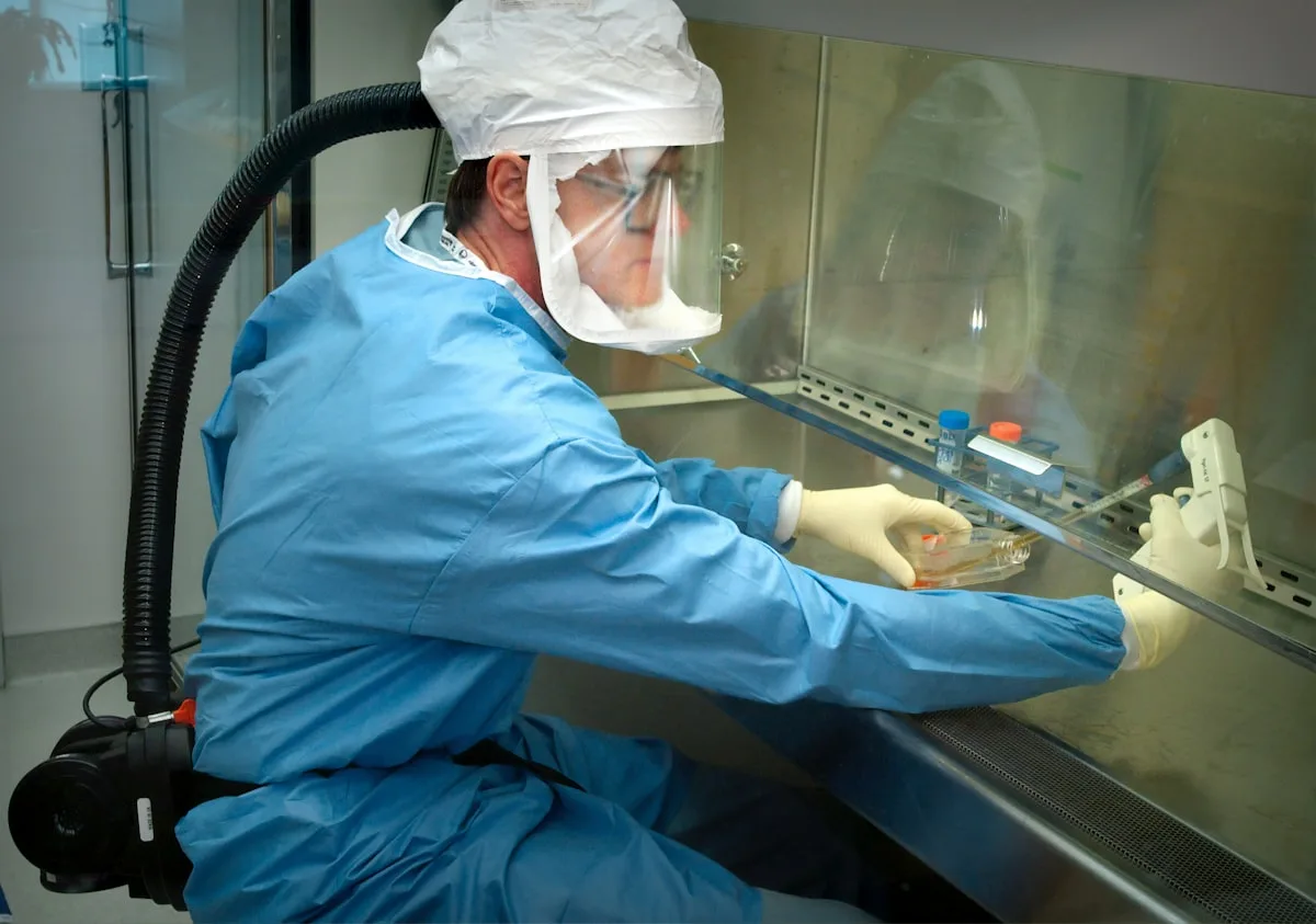 Healthcare worker in protective suit and mask operating laboratory equipment, photographed by the CDC — illustrative imagery for the Nebraska Biocontainment Unit and National Quarantine Unit that will monitor 17 American passengers returning from the MV Hondius hantavirus outbreak