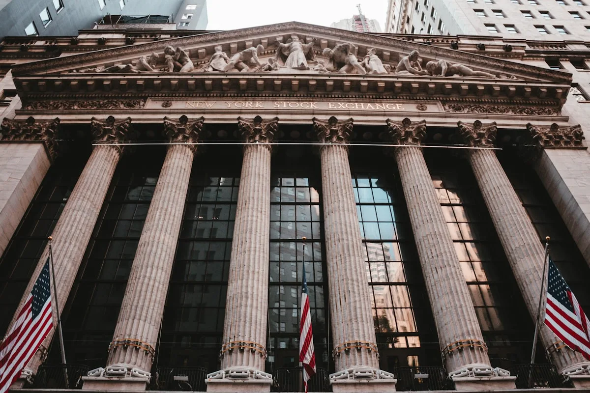 Stone façade of a Wall Street financial-district building draped with U.S. flags — illustrative imagery for Newsorga's reporting on Apollo Global Management's discussions, first reported by the Wall Street Journal on May 10–11, 2026, to sell its $3 billion MidCap Financial Investment Corp (MFIC) publicly listed business development company amid rising private-credit defaults.