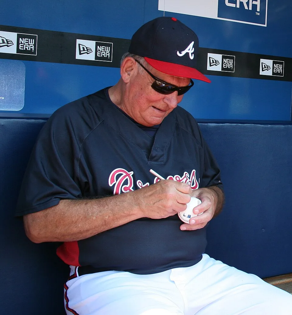 Bobby Cox signs an autograph for a fan in a cropped file photo from Commons (not from 2026).