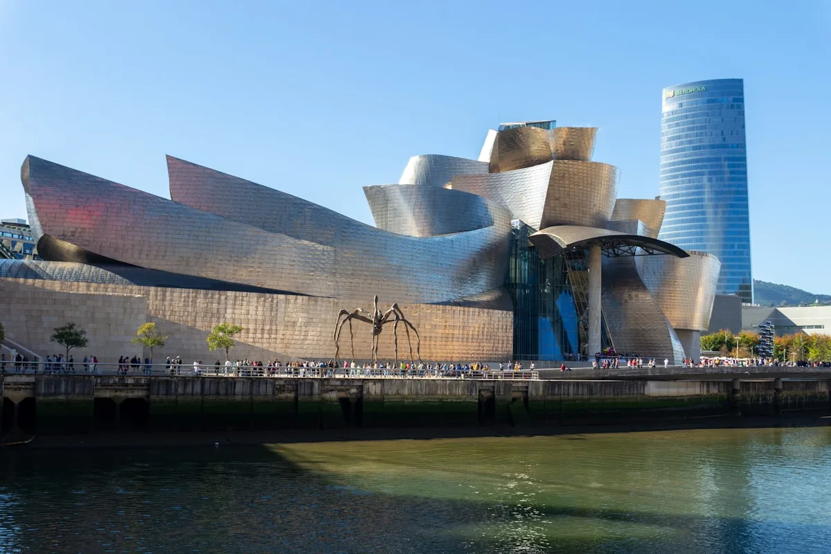 The titanium-clad Guggenheim Museum Bilbao seen from across the Nervión river — the 1997 Frank Gehry building credited with creating the 'Bilbao effect,' photographed as illustrative imagery for a five-months-on re-reading of Philip Kennicott's December 5, 2025 Washington Post column on Gehry's death at age 96.