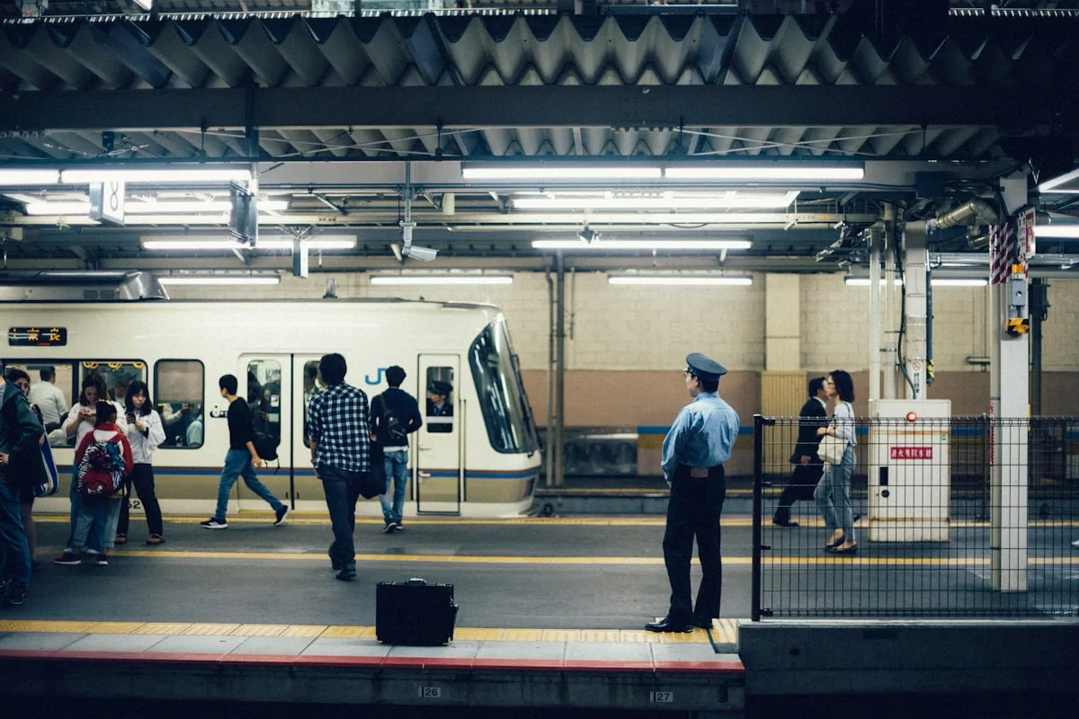 Commuters standing on a Japanese rail platform beside a white commuter train at dusk — illustrative imagery for the JR East Tokaido Line train that was halted at Kawasaki Station in Kanagawa Prefecture on the afternoon of May 10, 2026 after passengers reported an unknown substance was sprayed inside one of the carriages