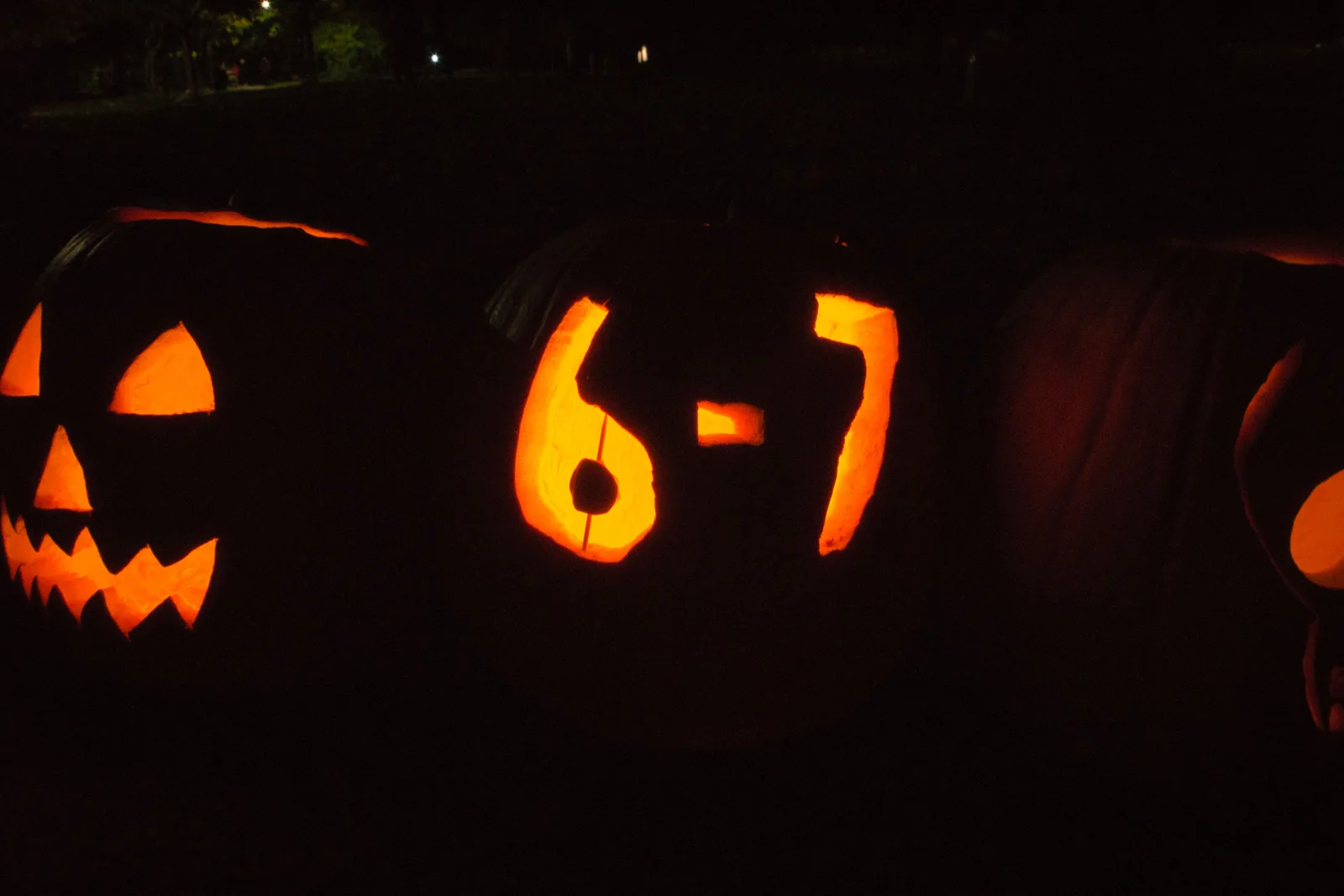 Nighttime photo in Toronto of lit jack-o'-lanterns and people in costume holding open palms in the viral "six-seven" hand gesture (Wikimedia Commons).